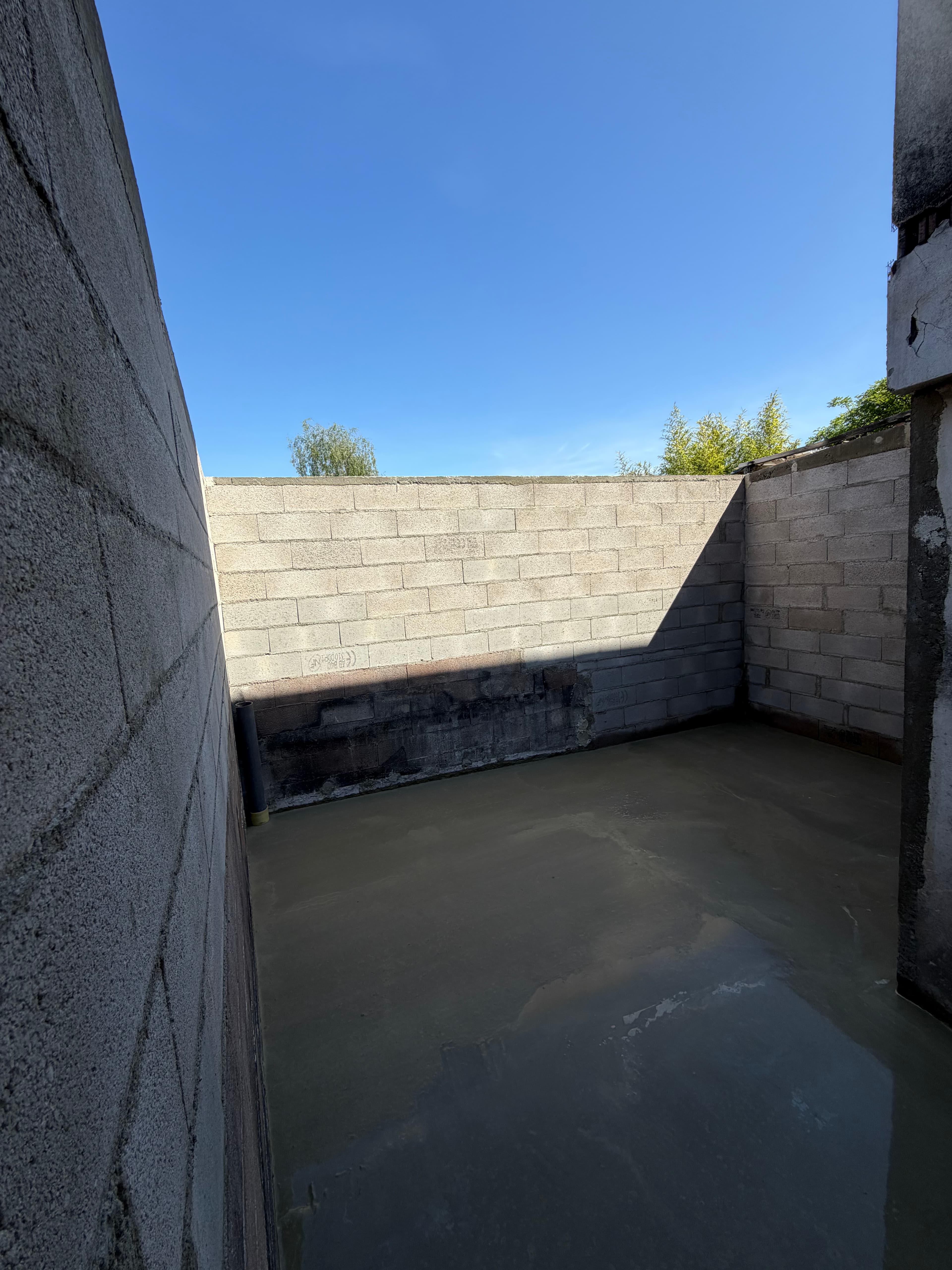 Dalle béton coulée et talochée, pente dirigée vers l'évacuation PVC en pied de mur.