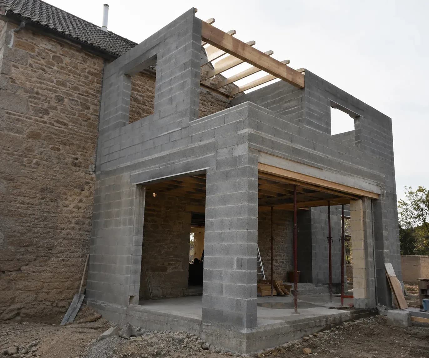 Extension en cours de construction, ossature en parpaings accolée à un bâtiment existant.